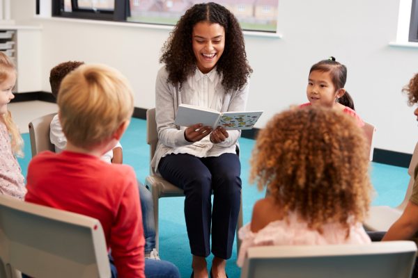Young teacher reading aloud to primary age pupils in a classroom