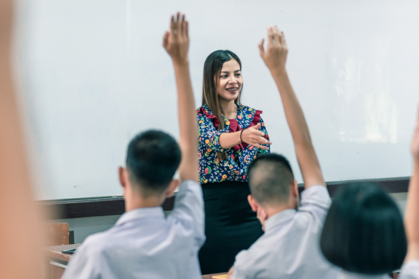 A teacher with two children with their hands in the air